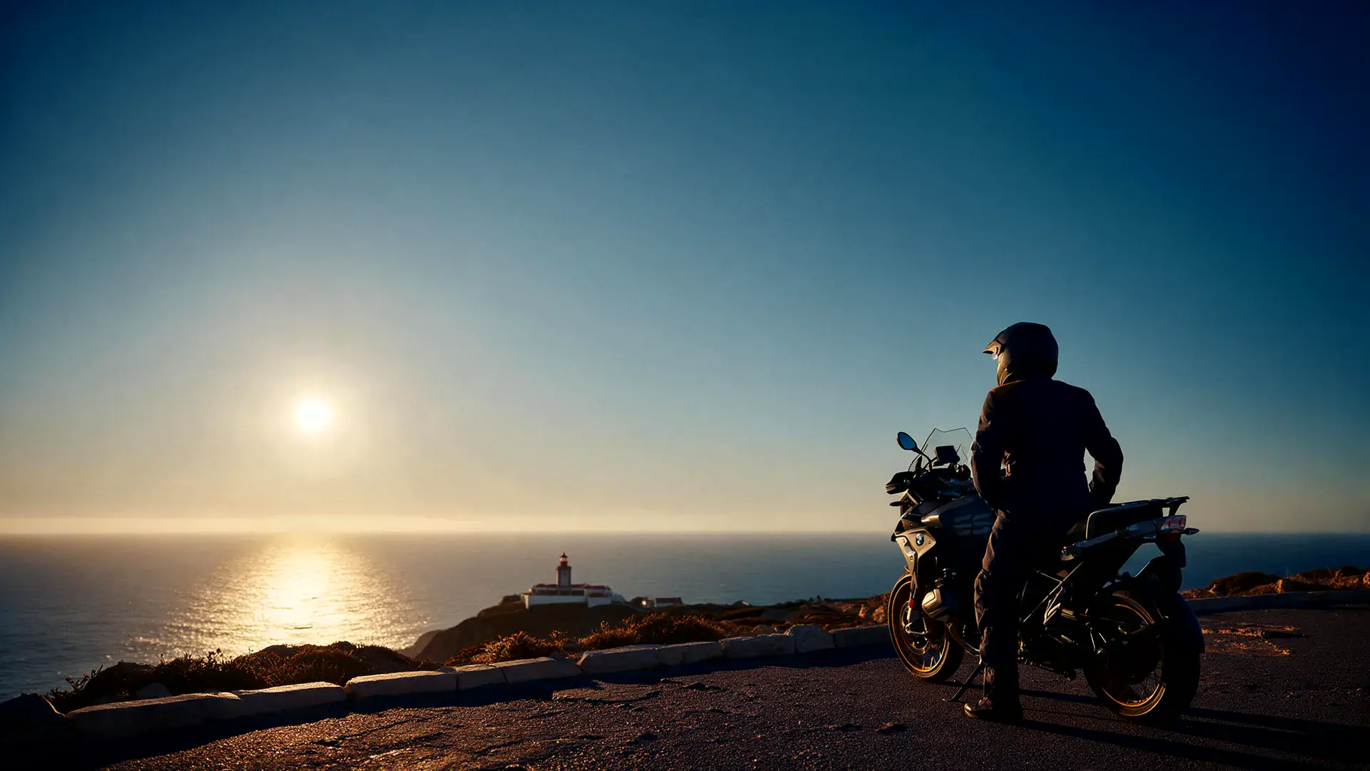 Piloto parado na moto à beira do penhasco do Cabo da Roca, com o farol e o Atlântico ao fundo